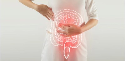 A imagem apresenta uma pessoa vestindo uma camiseta branca com as mãos posicionadas sobre o abdômen. Sobre a região abdominal, há uma ilustração translúcida do trato gastrointestinal, destacando o intestino grosso em uma tonalidade vermelha, sugerindo a presença de desconforto ou problema intestinal.